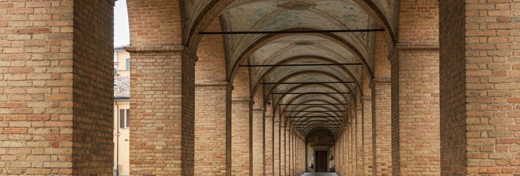 Receding brick arcade of round arches on square piers, faded painted cross vaults, iron tie rods and a dark wooden door at the far end
